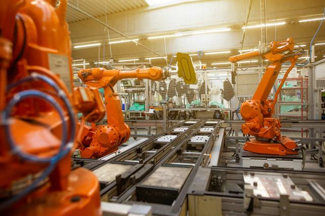 Orange industrial robot arms working on a factory assembly line.