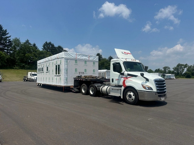 A tractor-trailer transporting a modular home on a flatbed.